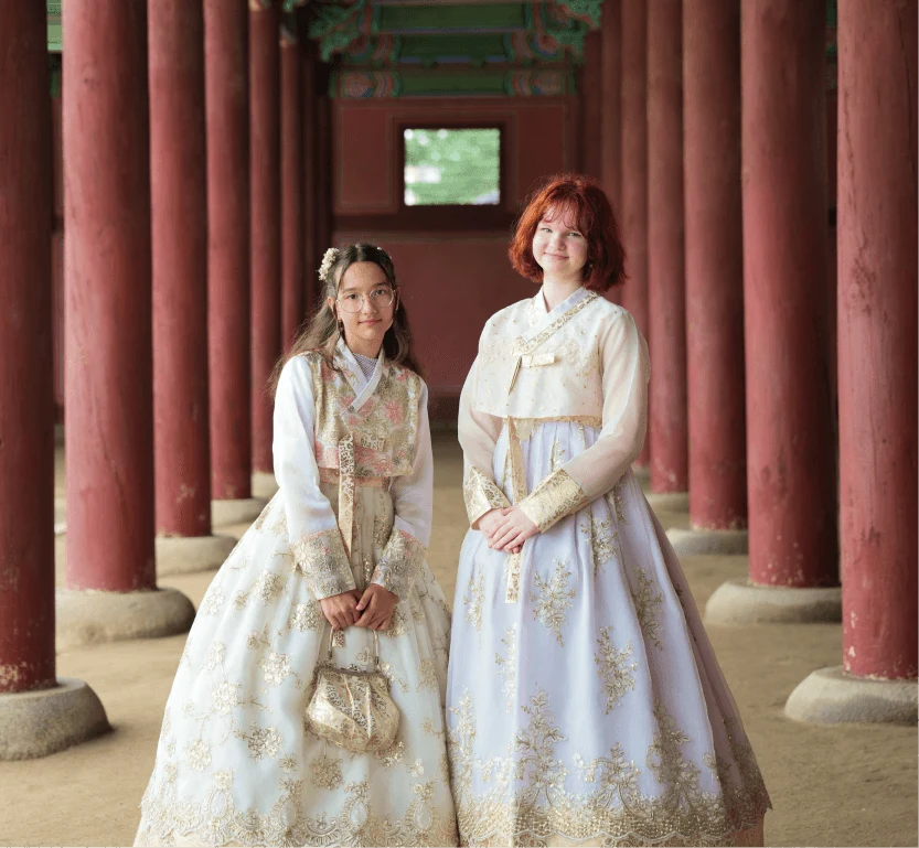 Two travelers in light-colored hanbok among palace columns