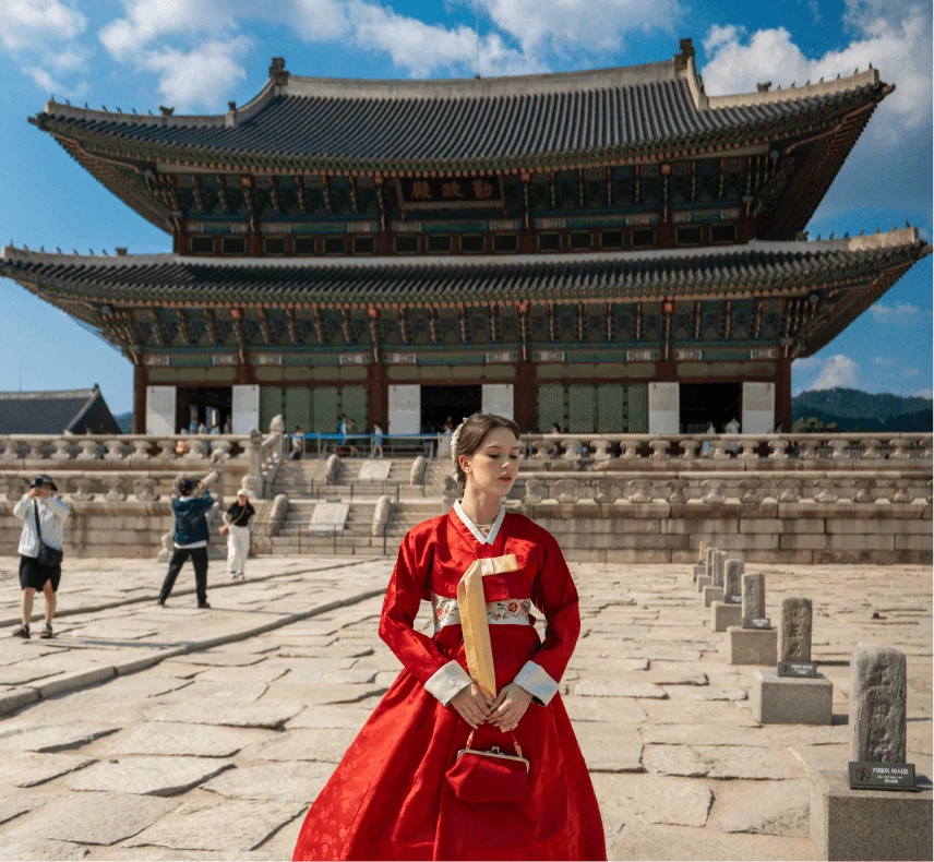 A traveler in a red hanbok in front of a Korean palace