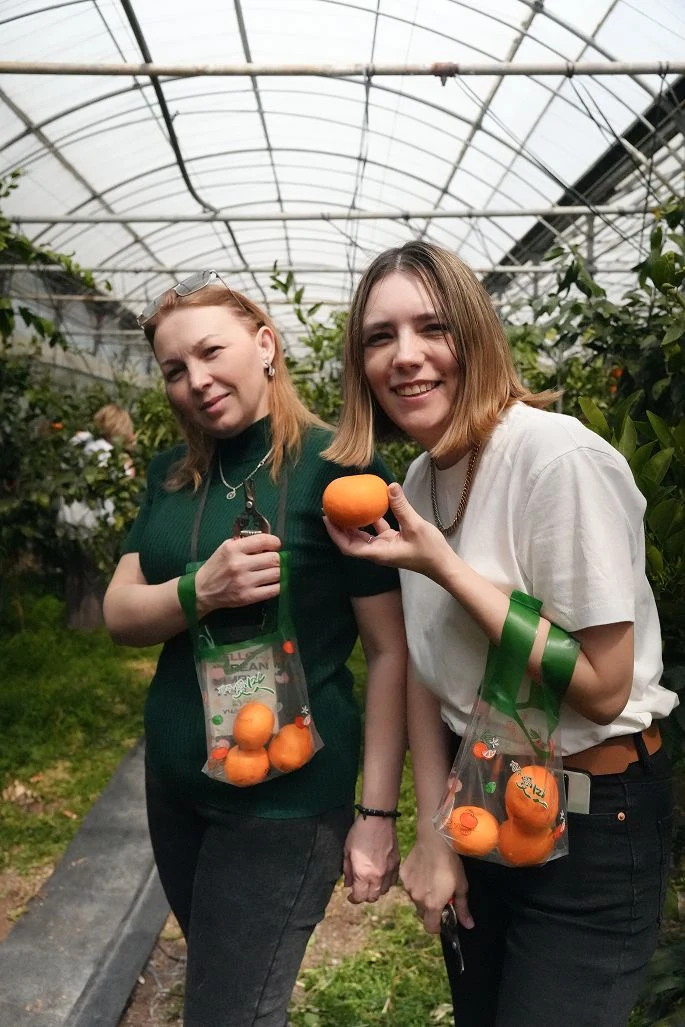 Two women with oranges in a greenhouse
