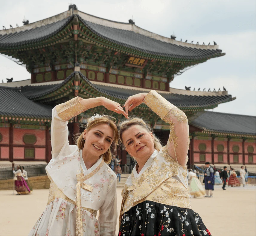 Two travelers in hanboks making a heart with their hands