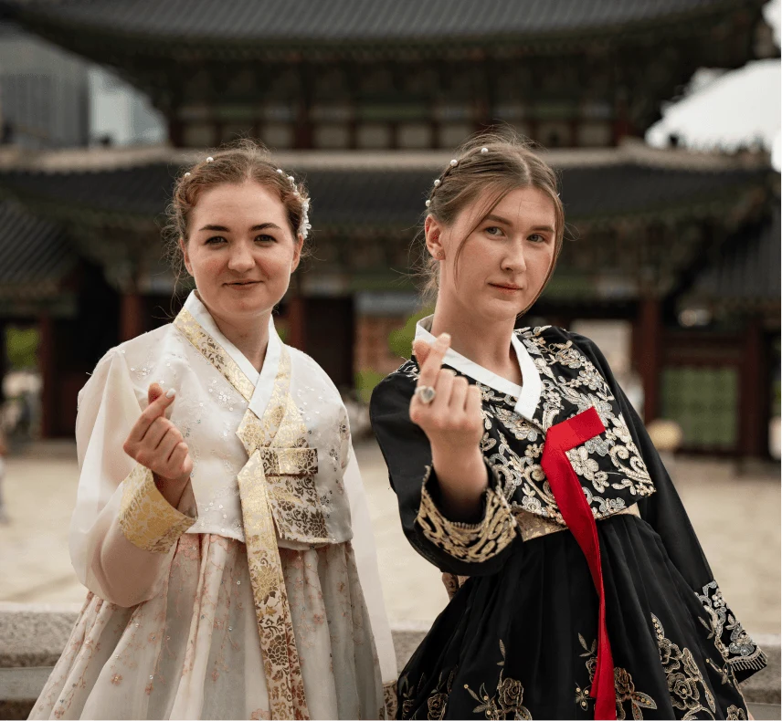 Two tourists in white and black hanboks making heart gestures