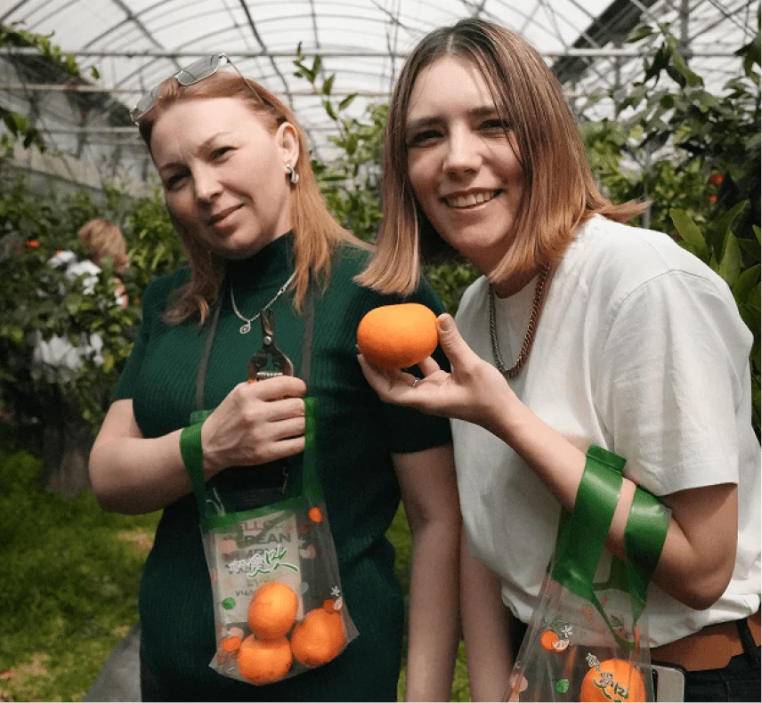 Two women with oranges in a greenhouse